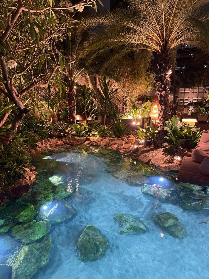 Lago ornamental iluminado à noite, com fundo de areia e pedras